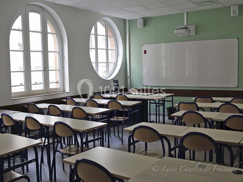 Salle de classe vide avec des tables et des chaises alignées, tableau blanc et grandes fenêtres arrondies.