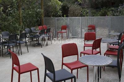 Terrasse extérieure avec des tables rondes et des chaises rouges et noires, entourée de végétation et de barrières…