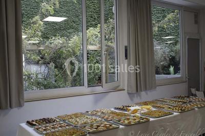 Terrasse extérieure avec des tables rondes et des chaises rouges et noires, entourée de végétation et de barrières…