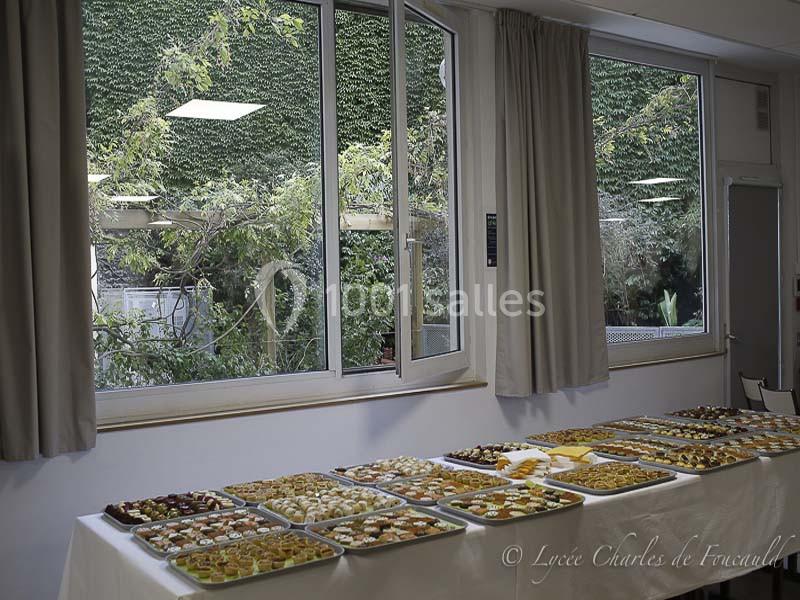 Table garnie de plateaux de petits fours et desserts variés, disposée près de grandes fenêtres donnant sur un jardin.