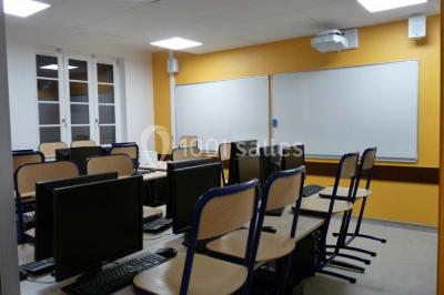 Terrasse extérieure avec des tables rondes et des chaises rouges et noires, entourée de végétation et de barrières…