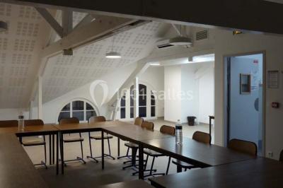 Terrasse extérieure avec des tables rondes et des chaises rouges et noires, entourée de végétation et de barrières…