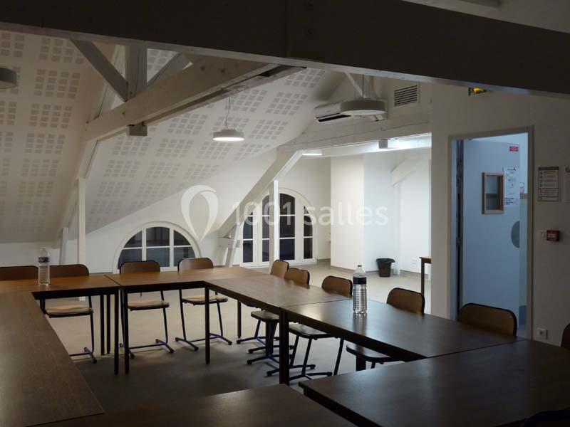 Salle de réunion lumineuse avec poutres apparentes, tables en U, chaises et fenêtres en arche.