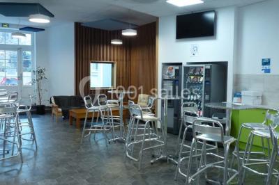 Terrasse extérieure avec des tables rondes et des chaises rouges et noires, entourée de végétation et de barrières…