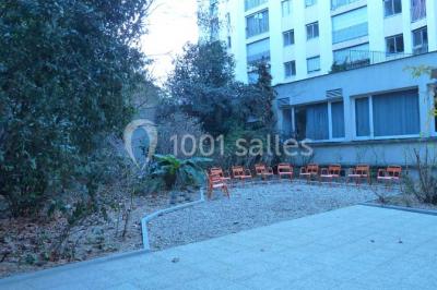 Terrasse extérieure avec des tables rondes et des chaises rouges et noires, entourée de végétation et de barrières…