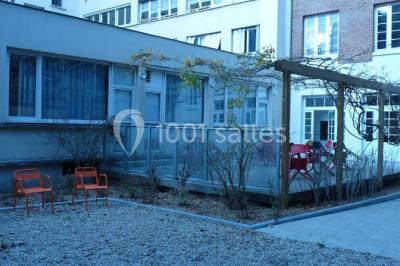 Terrasse extérieure avec des tables rondes et des chaises rouges et noires, entourée de végétation et de barrières…