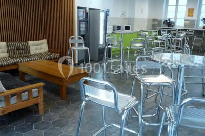 Terrasse extérieure avec des tables rondes et des chaises rouges et noires, entourée de végétation et de barrières…