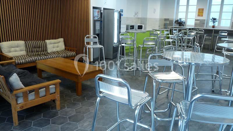 Salle de pause avec tables, chaises métalliques, canapés, distributeurs automatiques et micro-ondes.
