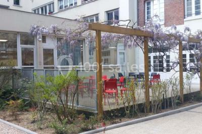 Terrasse extérieure avec des tables rondes et des chaises rouges et noires, entourée de végétation et de barrières…