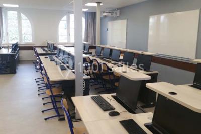 Terrasse extérieure avec des tables rondes et des chaises rouges et noires, entourée de végétation et de barrières…