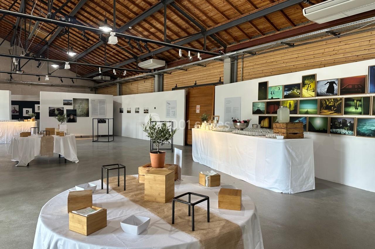 Salle d'exposition avec des photographies accrochées aux murs et des tables décorées de boîtes en bois et d'objets.