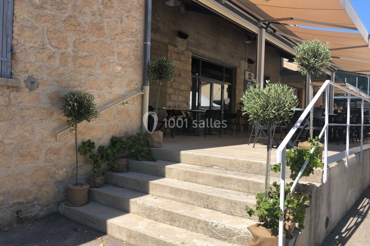 Entrée d'une terrasse de restaurant avec des marches en pierre, des plantes en pot et un auvent beige.