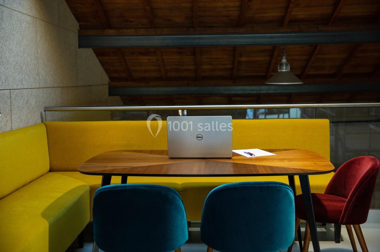 Ordinateur portable posé sur une table en bois entourée de chaises colorées dans une pièce au plafond en bois.