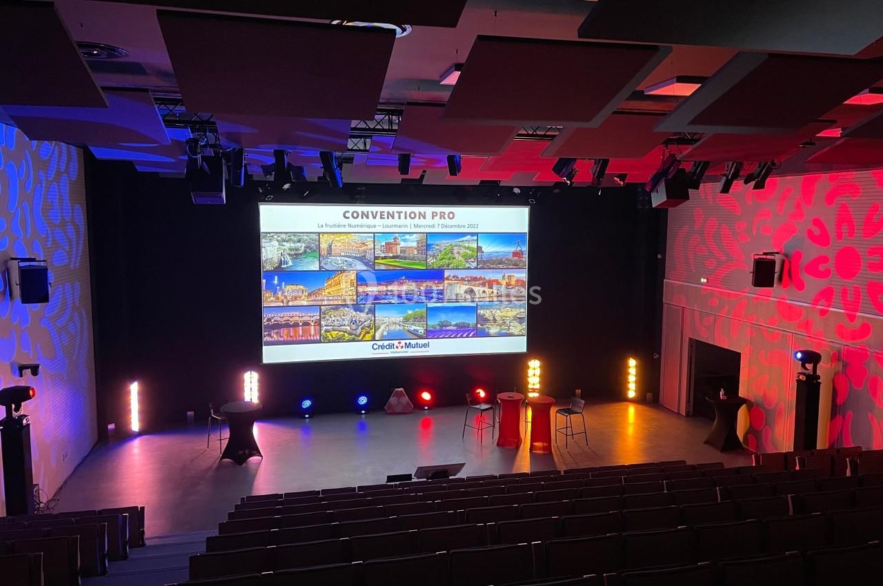 Salle de conférence vide avec un écran projetant des images et des lumières colorées illuminant la scène.