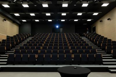 Salle de réunion avec tables et chaises disposées en U, grand écran blanc, plantes et buffet en arrière-plan.