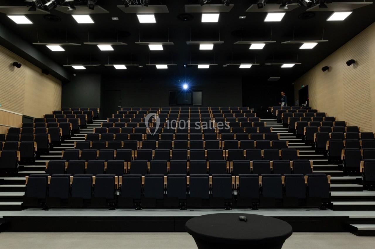 Salle de conférence moderne avec rangées de sièges noirs vides et éclairage au plafond.