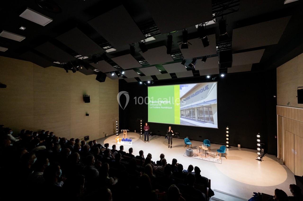 Salle de conférence avec un public, une présentation projetée sur écran et deux intervenants sur scène.