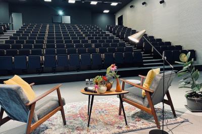 Salle de réunion avec tables et chaises disposées en U, grand écran blanc, plantes et buffet en arrière-plan.