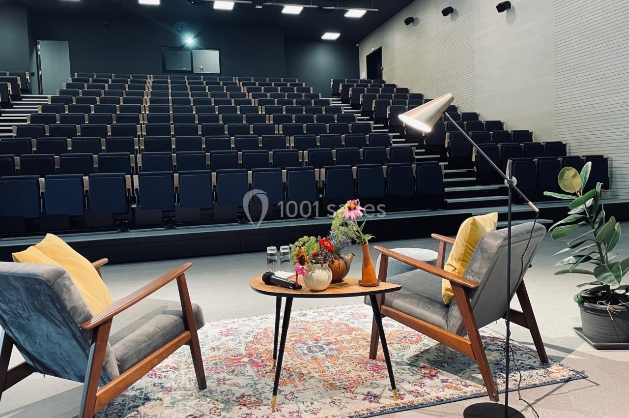 Deux fauteuils et une table basse avec des fleurs, disposés sur un tapis devant un amphithéâtre vide.