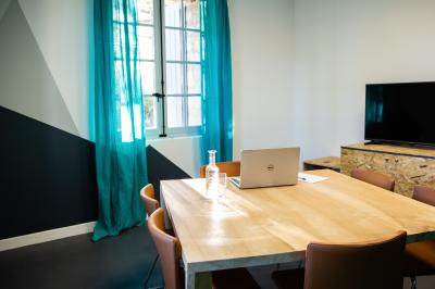 Salle de réunion avec tables et chaises disposées en U, grand écran blanc, plantes et buffet en arrière-plan.