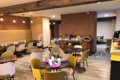 Un vase de fleurs sur une table en bois dans une salle avec poutres apparentes, un panneau ’Bienvenue’ au premier plan.