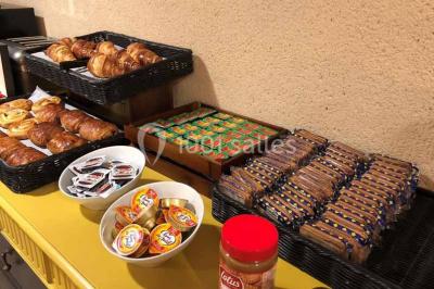 Un vase de fleurs sur une table en bois dans une salle avec poutres apparentes, un panneau ’Bienvenue’ au premier plan.