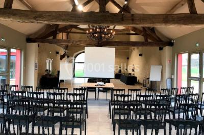 Un vase de fleurs sur une table en bois dans une salle avec poutres apparentes, un panneau ’Bienvenue’ au premier plan.