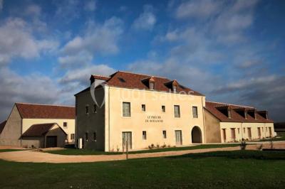 Un vase de fleurs sur une table en bois dans une salle avec poutres apparentes, un panneau ’Bienvenue’ au premier plan.