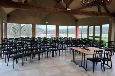 Un vase de fleurs sur une table en bois dans une salle avec poutres apparentes, un panneau ’Bienvenue’ au premier plan.