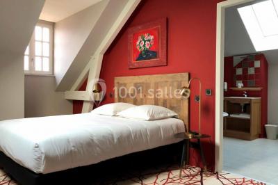 Un vase de fleurs sur une table en bois dans une salle avec poutres apparentes, un panneau ’Bienvenue’ au premier plan.