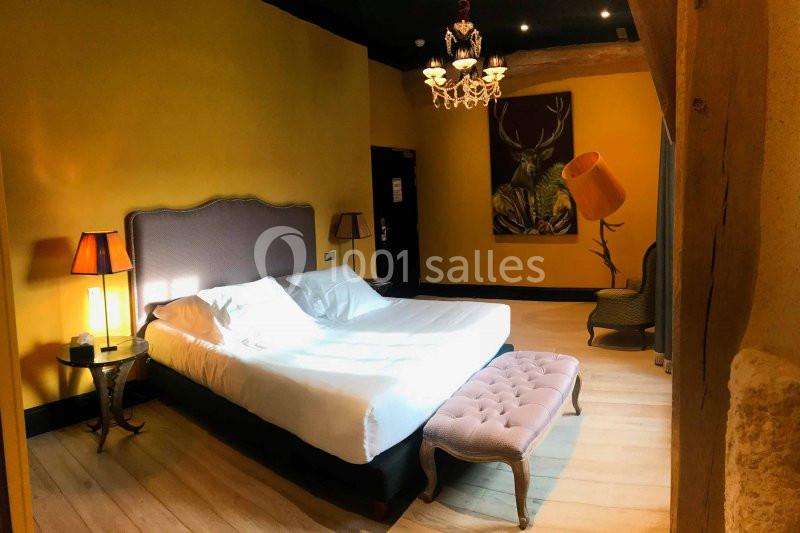 Chambre lumineuse avec murs jaunes, lit double, banc capitonné, lampes et tableau représentant un cerf.