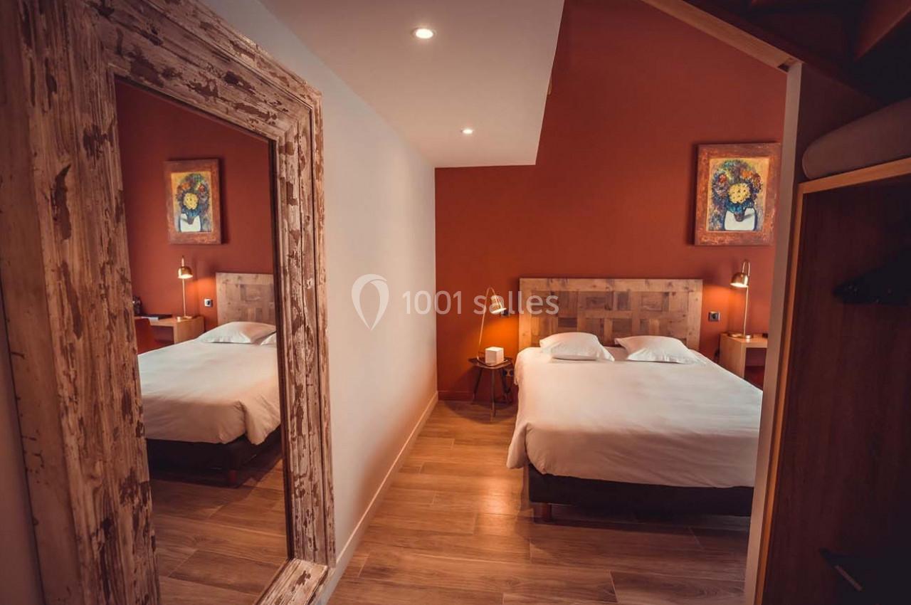 Chambre avec lit double, murs rouges, parquet, miroir encadré en bois et tableaux décoratifs.