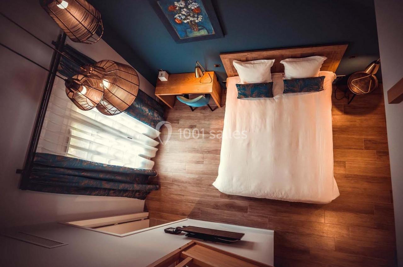 Vue aérienne d'une chambre avec un lit double, un bureau en bois, des luminaires suspendus et un sol en parquet.