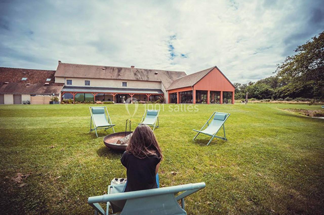 Une personne assise sur une chaise longue face à un grand bâtiment entouré d'une pelouse et de chaises longues.