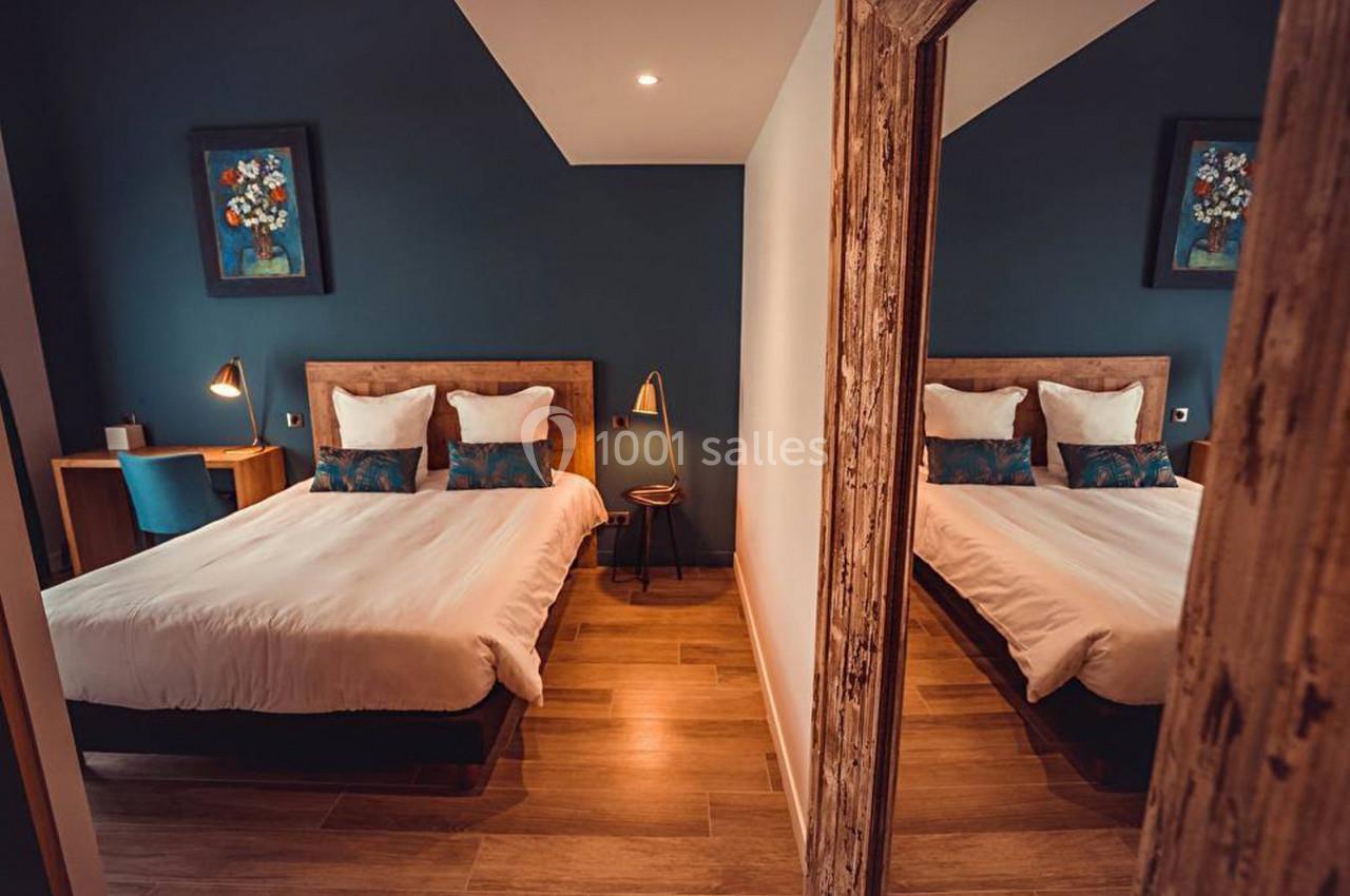 Chambre avec lit double, mur bleu, bureau en bois, lampe de chevet et miroir reflétant l'ensemble.