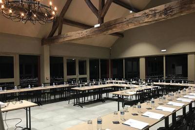 Un vase de fleurs sur une table en bois dans une salle avec poutres apparentes, un panneau ’Bienvenue’ au premier plan.