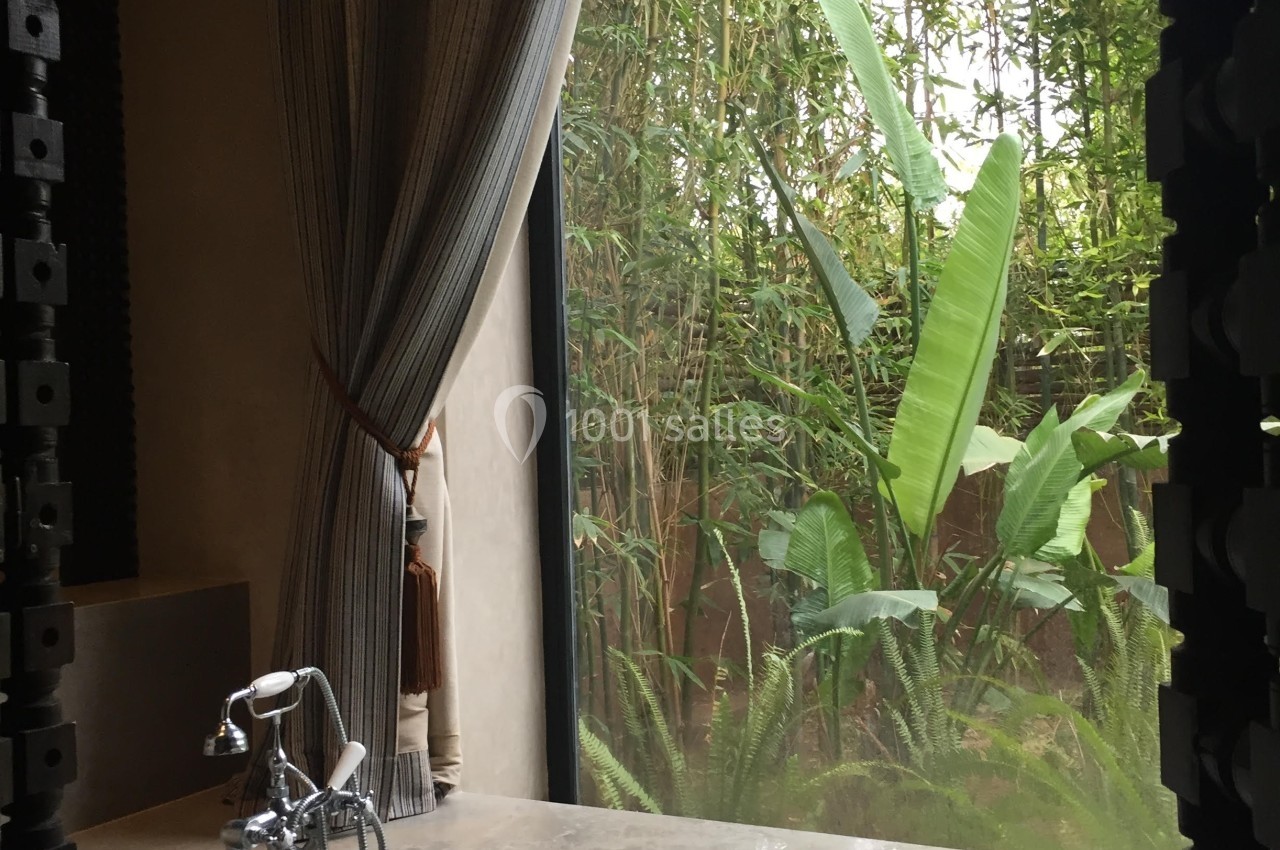 Vue d'une salle de bain avec une baignoire près d'une grande fenêtre donnant sur un jardin tropical verdoyant.