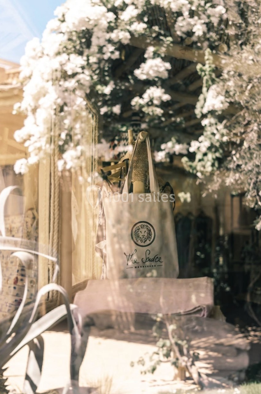 Sac en toile beige posé sur une chaise, entouré de plantes et de fleurs blanches dans un décor lumineux.