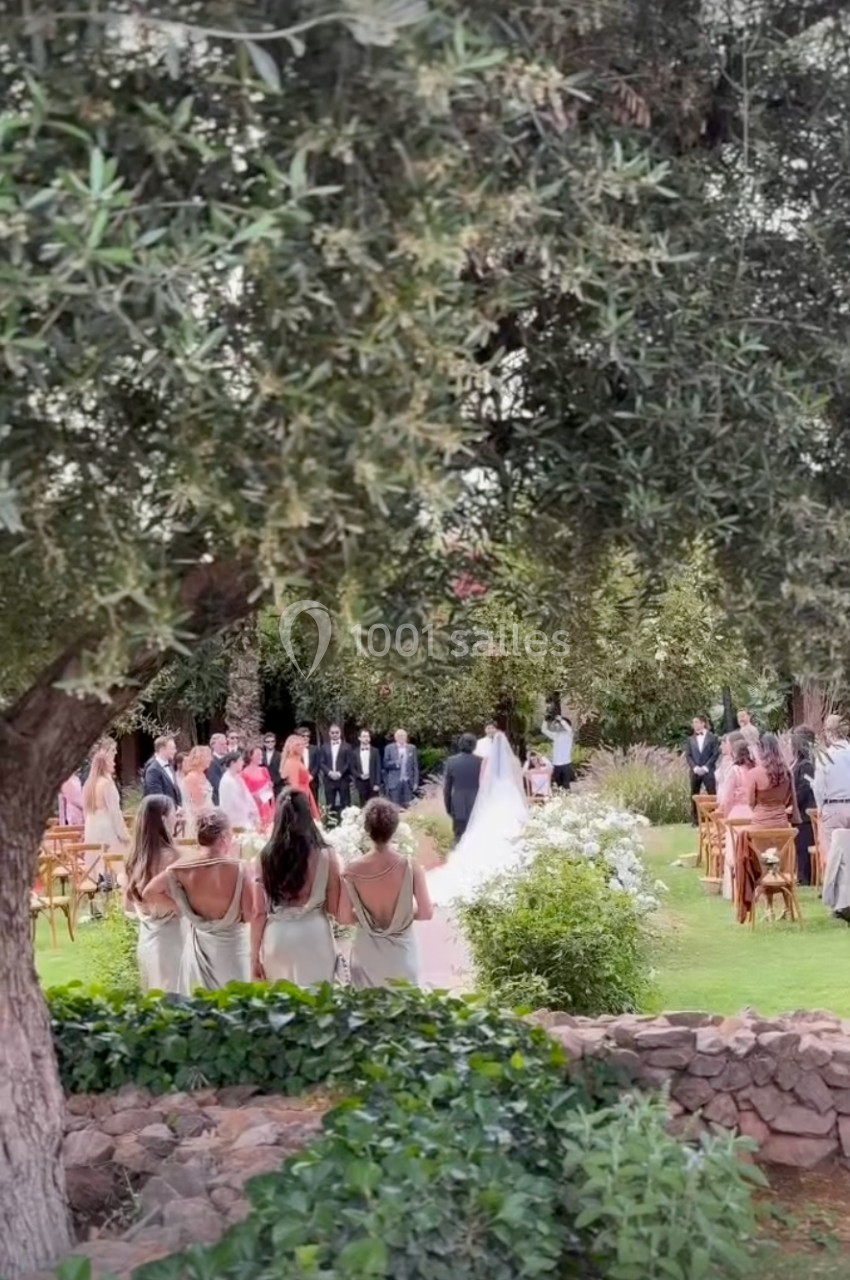 Cérémonie de mariage en plein air avec des invités debout autour des mariés dans un jardin verdoyant.