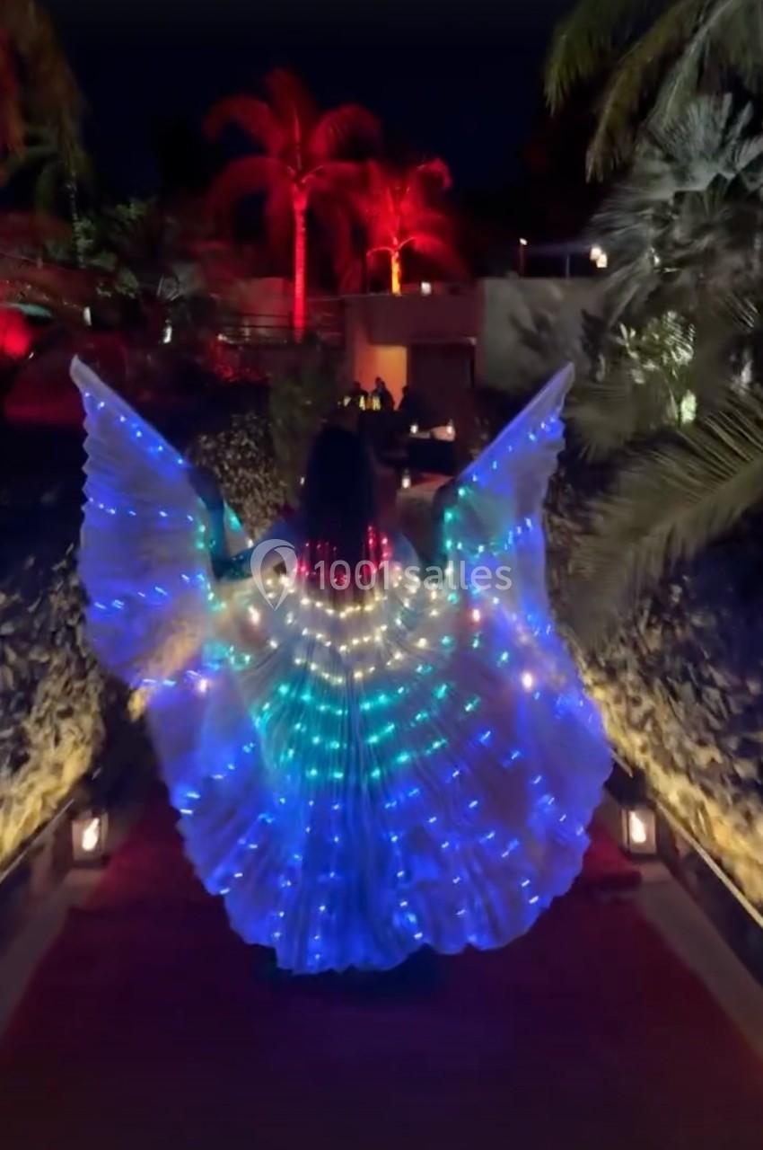 Personne portant une robe lumineuse avec des motifs colorés, avançant sur un chemin éclairé entouré de végétation tropicale.