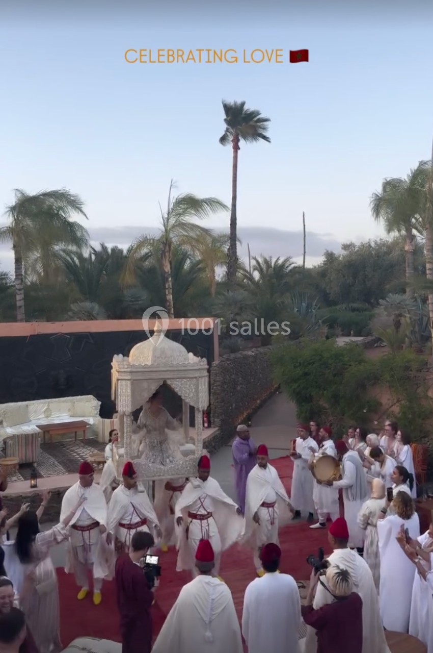 Un groupe de personnes en tenues traditionnelles danse autour d'un palanquin décoré dans un jardin exotique.