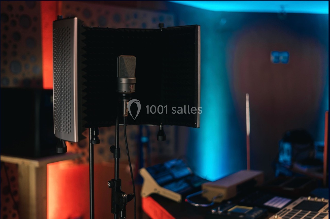 Microphone sur pied avec écran acoustique dans un studio d'enregistrement éclairé par des lumières colorées.