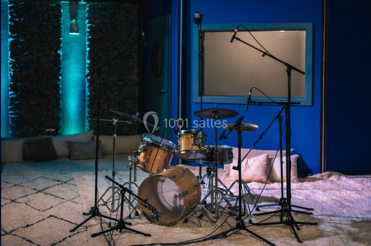 Batterie installée dans un studio d'enregistrement avec tapis au sol, murs bleus et éclairage tamisé.