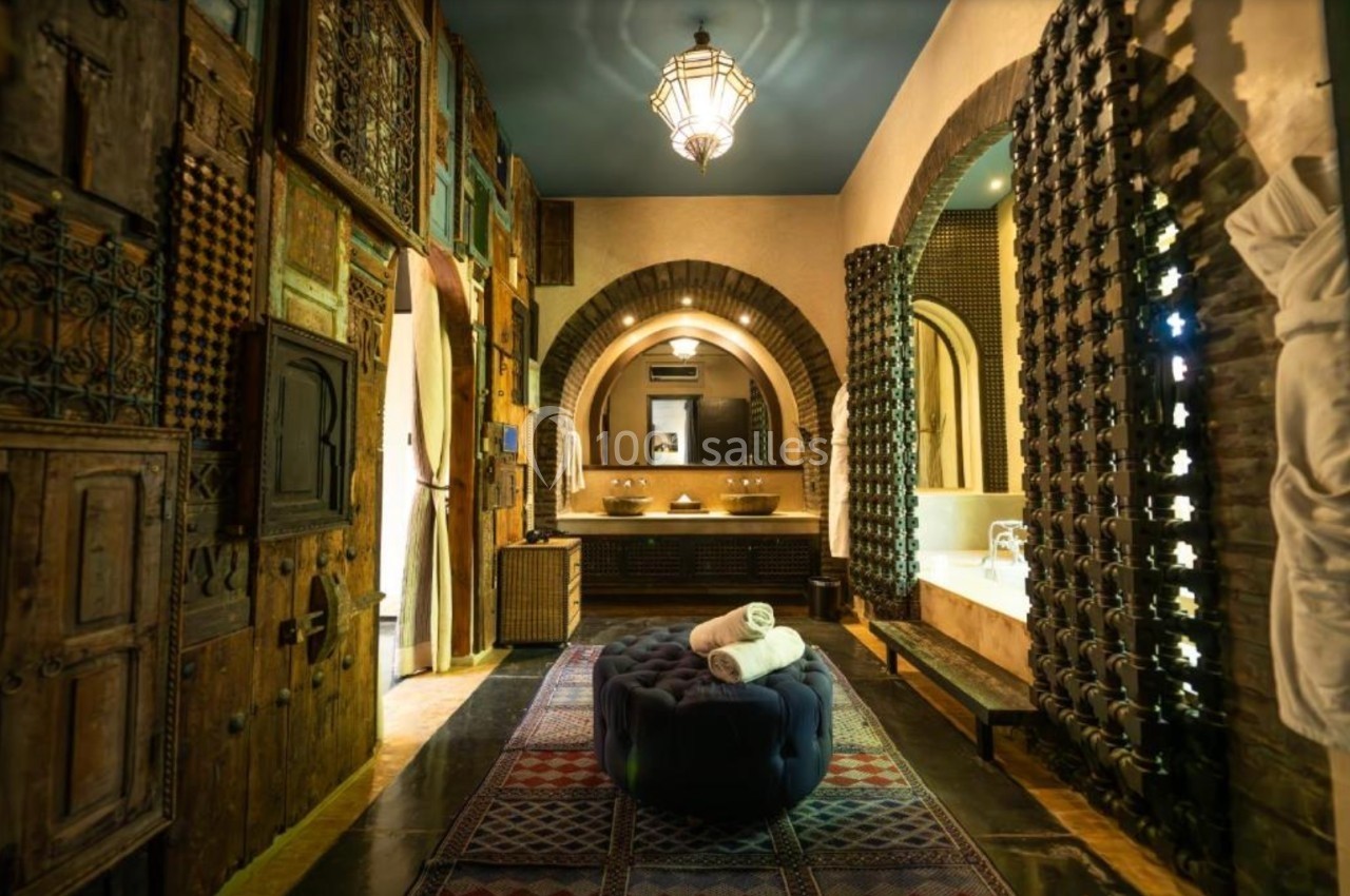 Salle de bain au style marocain avec arches, murs ornés de bois sculpté, baignoire et lumière tamisée.