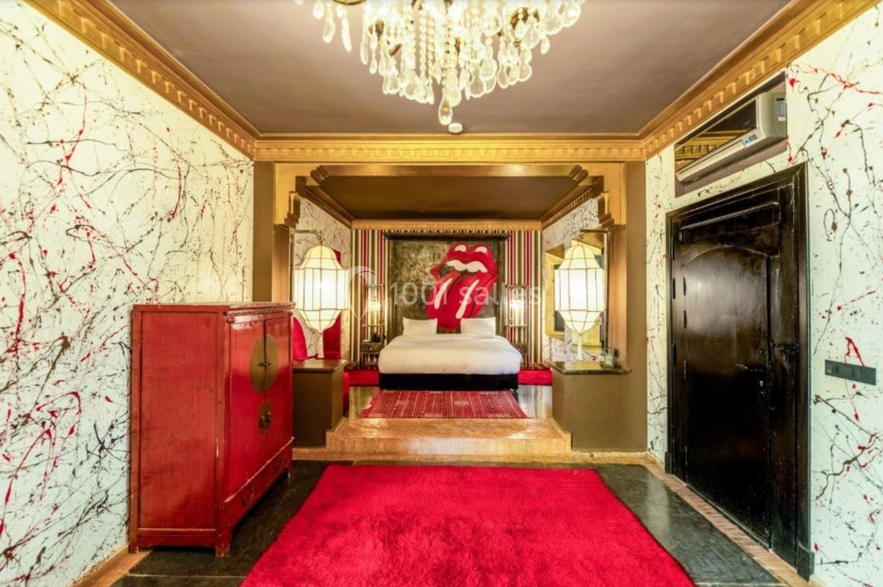 Chambre décorée avec un lit orné d'un motif de lèvres rouges, murs texturés et lustre en cristal.