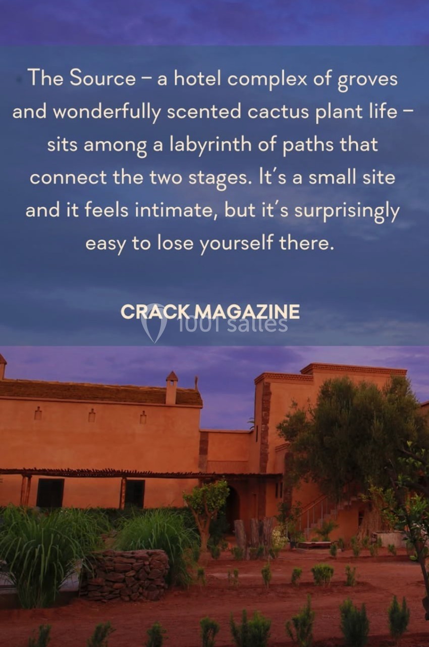 Bâtiments en terre cuite entourés de végétation, sous un ciel violet au coucher du soleil.