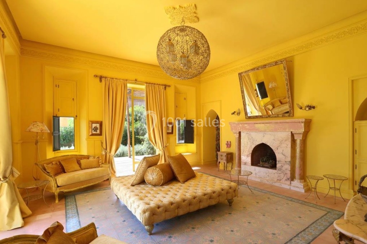 Salon lumineux aux murs jaunes, décoré avec des meubles élégants, un lustre imposant et une cheminée en marbre.