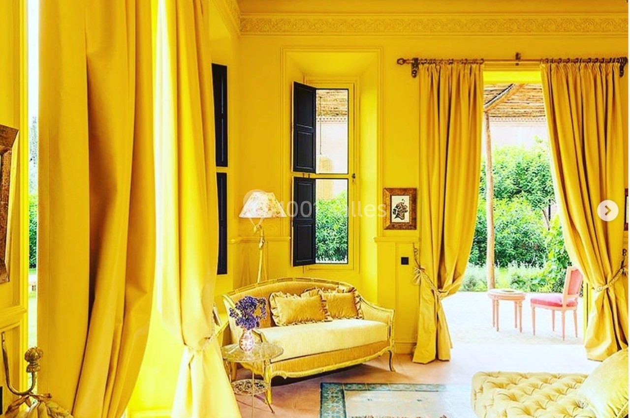 Salon lumineux avec murs, rideaux et mobilier jaunes, ouvert sur un jardin verdoyant visible à travers une porte vitrée.