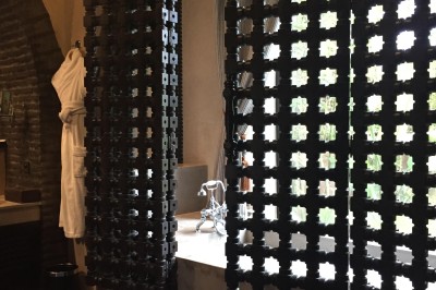 Cloison décorative ajourée en bois sombre devant une baignoire avec robinetterie métallique, lumière naturelle en arrière…