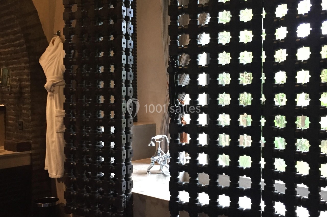 Cloison décorative ajourée en bois sombre devant une baignoire avec robinetterie métallique, lumière naturelle en arrière…